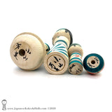 A photo showing the signature of kokeshi artist Yoshimi Koyama. The photo appears on the base of a one-of-a-kind modern kokeshi doll. The doll has a peaceful expression and is made from nicely grained hardwood.