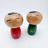 A Pair of Adorable Kokeshi Dolls by Hashime Takahashi. One Red, One Green. Both have peaceful yet joyful faces!