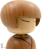 A closeup photo of an original, one-of-a-kind modern kokeshi doll by Isao Sasaki. Handmade from beautifully grained hardwood. A pretty kokeshi with a calm expression.