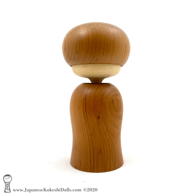 A rear view photo of an original, one-of-a-kind modern kokeshi doll by Isao Sasaki. Handmade from beautifully grained hardwood. A pretty kokeshi with a calm expression.