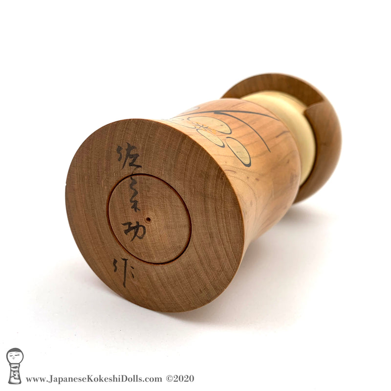 A photo showing the signature of kokeshi artist Isao Sasaki. The signature appears on the base of a one-of-a-kind kokeshi doll made from beautifully grained hardwood.