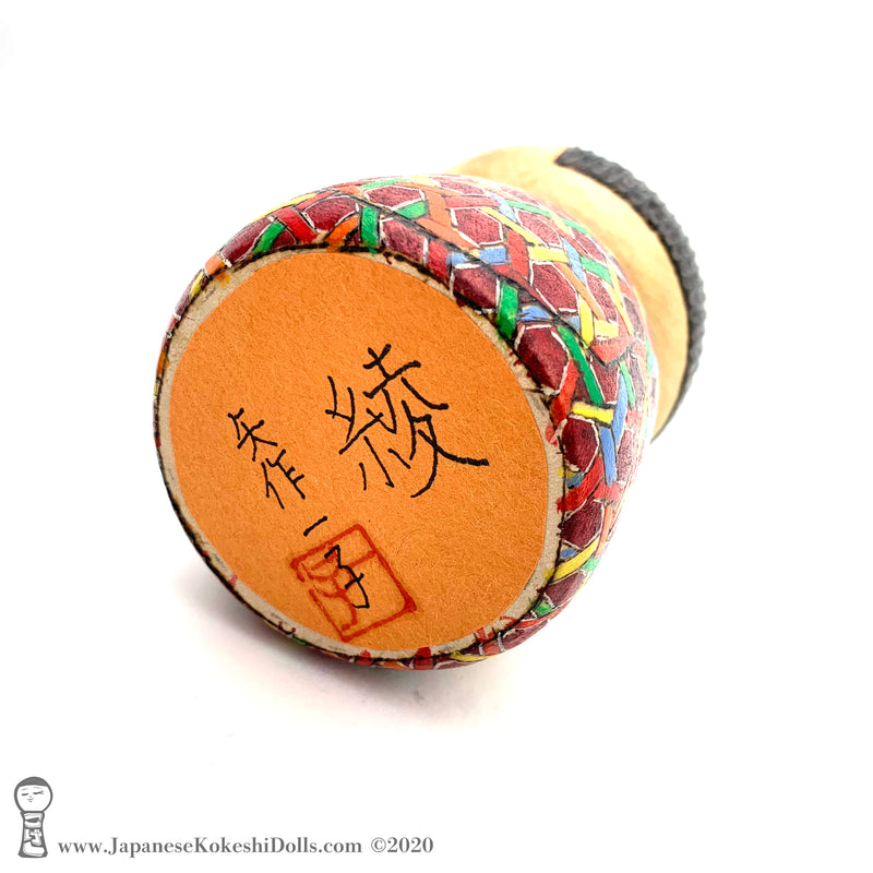A photo showing the signature of kokeshi artist Kazuko Yahagi. The photo appears on the base of a one-of-a-kind modern kokeshi doll. The doll has a peaceful expression and is made from nicely grained hardwood.
