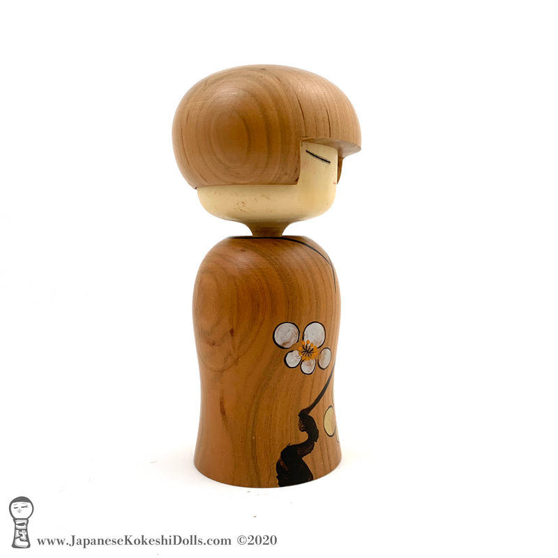 A side view photo of an original, one-of-a-kind modern kokeshi doll by Isao Sasaki. Handmade from beautifully grained hardwood. A pretty kokeshi with a calm expression.